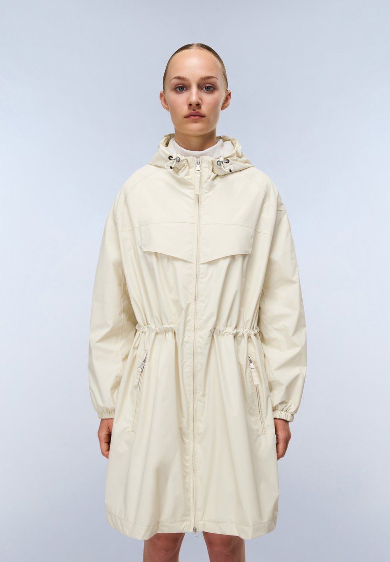 Cappotto impermeabile beige chiaro con cappuccio regolabile, zip completa, due tasche con zip e polsini elasticizzati con un design in vita cinch.