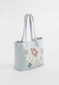 Sac fourre-tout bleu clair en cuir avec des applications florales multicolores. Il possède des poignées doubles et un dessus ouvert.