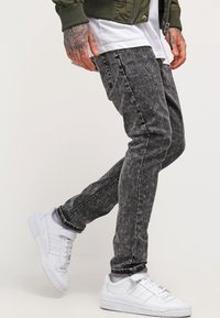 Gray, faded jeans with a slim fit and subtle texture detail, paired with white sneakers and an olive green bomber jacket.