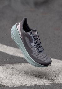 Baskets de sport grises avec un dessus texturé et respirant et une semelle extérieure vert clair. Elles sont dotées de lacets et d'un design épuré pour des performances optimales.