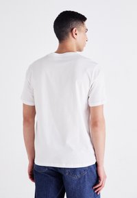 Hvit bomulls t-skjorte med korte ermer, rund hals og en avslappet passform. Enkelt design uten synlige logoer eller mønstre. Vist bakfra.