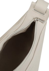 Interno di una borsa a tracolla in pelle beige chiaro con zip. Texture liscia, senza motivi. Il cursore della zip presenta un'etichetta con il marchio "RYŁKO".