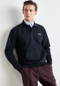 Sweatshirt azul marinho de gola redonda com um bolso frontal, feito de tecido macio. Apresenta um pequeno logotipo "BOSS" no peito, combinado com calças bordô.