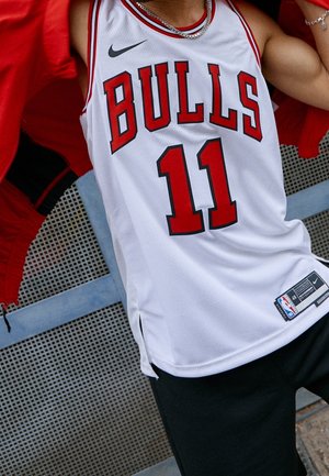 Persona che indossa una maglia da basket bianca dei Chicago Bulls con il numero 11 e una collana d'argento, solleva una giacca rossa.