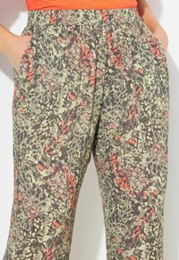 Pantaloni larghi e stretch con un motivo astratto verde, grigio e corallo. Vita elastica con tasche laterali. Tessuto leggero.