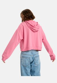 Skrojony hoodie w jasnoróżowym kolorze, z długimi rękawami, teksturowanym materiałem oraz kapturem. Połączony z jasnoniebieskimi dżinsami.