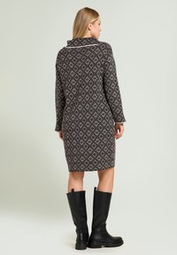 Zwart- en roomkleurige knielange jurk met patroon, een kraag, een textuurgebreide stof en lange mouwen, gecombineerd met hoge zwarte laarzen.