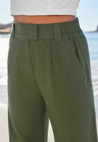 Pantalons à taille élastique vert olive avec poches latérales, fabriqués en tissu léger avec une texture subtile.