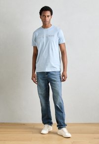 Lichtblauwe katoenen t-shirt met ronde hals en geborduurde tekst "ANTONY MORATO", gecombineerd met klassieke blauwe denim jeans en witte sneakers.