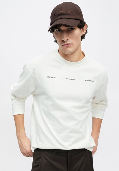 T-shirt branca de manga comprida com texto impresso. Apresenta gola redonda e corte descontraído. Combinada com um boné castanho com a inscrição "HOLZWEILER".