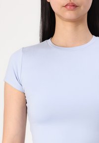 T-shirt de manga curta azul claro com decote redondo, feito de um tecido liso e elástico. Apresenta um design minimalista e uma forma ajustada.