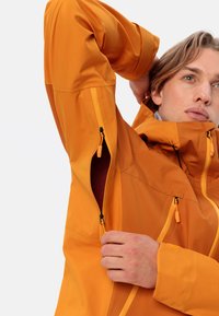 Oranje waterdichte jas met ritszakken, verstelbare manchetten en een hoge kraag. Getextureerde stof verhoogt de duurzaamheid en het comfort.