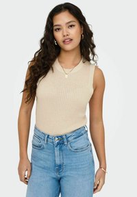 Beige geribbelde mouwloze top gecombineerd met hoogopgetrokken lichtblauwe jeans. Geassorteerd met een gouden ketting en oorbellen met ronde hoops.