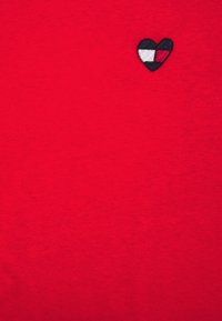 Červený pletený svetr se malým vyšívaným logo srdce v námořnické modři, bílé a černé barvě. Hladká textura, kulatý výstřih, žádné viditelné švy.