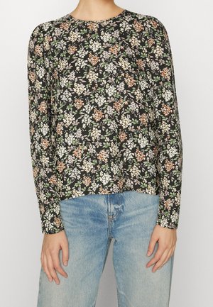 Długa bluzka z długim rękawem w kwiatowy wzór w kolorze czarnym z białymi, pomarańczowymi i zielonymi kwiatami. Okrągły dekolt i luźny fason, zestawiona z jasnoniebieskimi dżinsami.