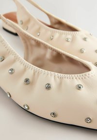 Beige nahkamateriaalista valmistetut ballerinat, joissa on joustavat reunat, koristeltu hopeisilla strasseilla, pyöreällä varpaalla ja littealla pohjalla.