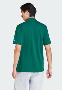 Green short-sleeve polo shirt made from cotton, featuring a simple design and a collar, with logo detail on the left sleeve.