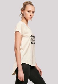 Short-sleeve, light beige t-shirt with a round neckline and black printed text, paired with black leggings. Slightly longer back hem.