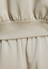 Bežna tkanina s mekanom teksturom i elastičnom trakom za struk. Nabrani detalj na šavu stvara efekt drapiranja. Glatki, rastezljivi materijal.