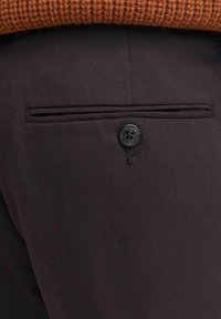 Pantalones ajustados de color marrón oscuro con una cinturilla texturizada y un solo bolsillo trasero con un detalle de botón negro.