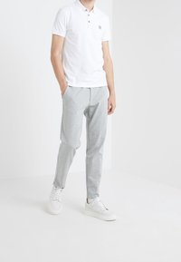 Valkoinen polo-paita, jossa on kolme nappia, harmaat verkkarit sivu-urilla ja valkoiset tennarit. Minimalistinen muotoilu, istuva siluetti.