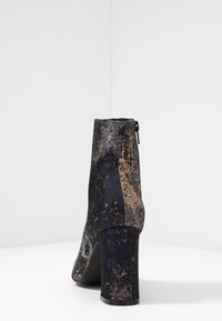 Botte à talon en tissu texturé, avec un motif bleu et or, bout rond, et une fermeture éclair à l'arrière.