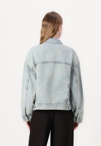 Light blue denim jacket featuring oversized design, visible stitching, and tonal "Hugo" lettering pattern across the back.