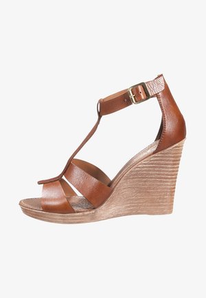 Brązowy skórzany sandał na koturnie z teksturowanym obcasem, z krzyżującymi się paskami i paskiem wokół kostki zapinanym na złotą klamrę.