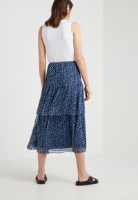 Dlouhá, vrstvená sukně v tmavě modré barvě s bílým květinovým vzorem; vyrobena z lehké, splývavé tkaniny. V kombinaci s upnutým bílým tílkem a černými sandály.