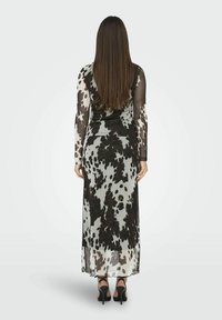Robe maxi à manches longues en tissu transparent avec un motif cow en noir et blanc. La robe a une coupe ajustée et un ourlet fluide et doux.
