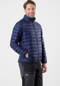 Dunkelblaue, isolierte Pufferjacke mit hohem Kragen, Reißverschluss und gestepptem Design. Verfügt über zwei seitliche Taschen und ein Logo auf der Brust.