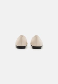 Beige nahkakengät, joissa on sileä pinta, pyöristetty kärki, matala musta korko ja ompeluyksityiskohta takasaumassa. Minimalistinen muotoilu.