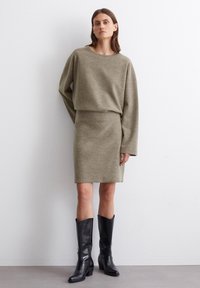 Robe pull en tricot vert olive avec une coupe décontractée, des manches longues et un col côtelé, associée à des bottes en cuir noir au-dessus du genou.