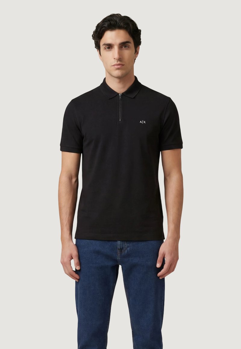 Homme portant un polo noir à manches courtes avec une fermeture éclair à l'avant et le logo A|X, associé à un jean bleu, debout devant un fond uni.