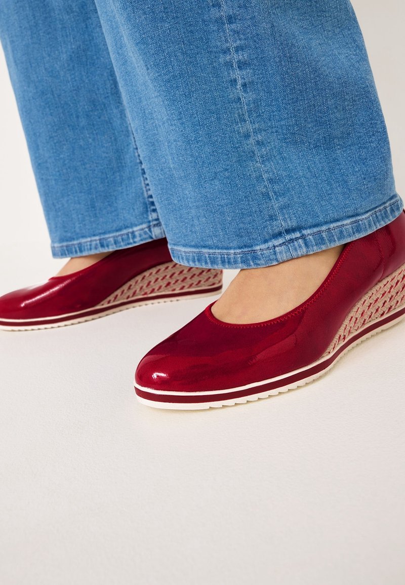 Des chaussures à talons compensés en cuir verni rouge présentent un bout rond et un motif tissé texturé sur le talon. La semelle extérieure est blanche avec un motif antidérapant.