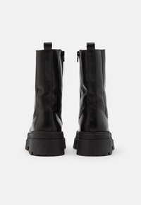 Botas de tobillo de cuero negro con suela gruesa, cierre de cremallera y tira de agarre en la parte posterior. Textura suave con detalles sutiles en los laterales.
