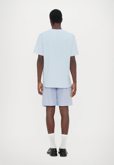 Lyseblå kortermet t-skjorte kombinert med stripete shorts. Shortsene har en liten gul lapp. Brukt med hvite sokker og svarte sko.