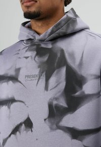 Lichtpaarse hoodie met een zwart abstract patroon. Voorzien van een capuchon met trekkoord en subtiele tekst "PRESENTED". Zachte textuur.