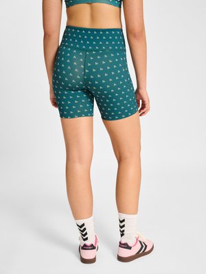 Vrouw draagt turquoise biker shorts met hoog taille en patroon, witte sokken met zwarte chevrons en roze sneakers, gezien van achteren.