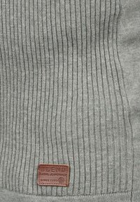 Grauer, gerippter Strickstoff mit einem Lederetikett, auf dem "Blend" steht, mit leichtem Glanz und strukturierter Oberfläche.