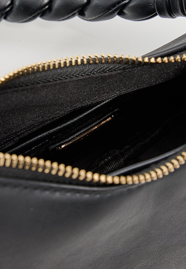 Binnenkant van een zwarte leren handtas met een gladde textuur, gouden rits en een insteekvak. Het ontwerp is minimalistisch met een geweven handvat.
