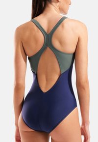 Traje de baño con diseño bicolor, parte superior verde y parte inferior azul marino. Tirantes cruzados en la espalda y espalda descubierta para mayor libertad de movimiento. Textura suave.