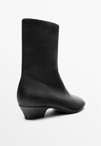 Černá kotníková bota s hladkým koženým povrchem, kulatou špičkou a nízkým, nenápadným podpatkem. Elegantní design s minimalistickou siluetou.