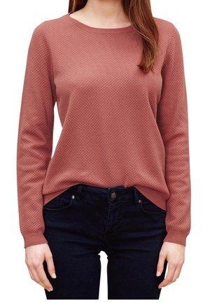 Pull en maille de couleur rouille avec un col rond et des manches longues, associé à un jean en denim foncé. Le tissu présente un motif en nid d'abeille discret.