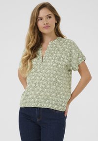 Blusa verde de manga corta con un patrón geométrico blanco, diseño de escote en V y un corte relajado, confeccionada en tejido ligero.