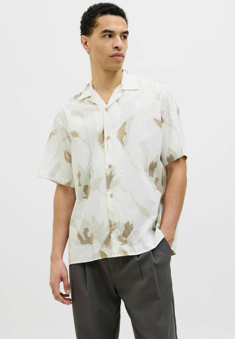 Camicia a maniche corte con bottoni in tessuto leggero, caratterizzata da un motivo floreale in tonalità tenui di beige e marrone. Colletto alla francese e vestibilità comoda.