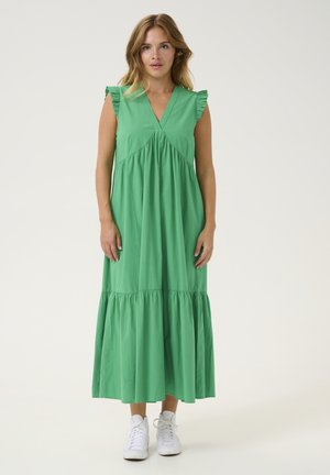 Grünes Maxikleid aus weichem Stoff, mit V-Ausschnitt, Rüschchenärmel und gestuftem Saum. Kombiniert mit weißen Sneakers.