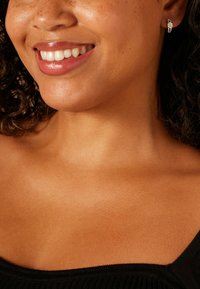 Zilveren oorringen met een sprankelend accent, gedragen door een persoon met een medium getinte huid en krullend haar, gekleed in een zwart topje.