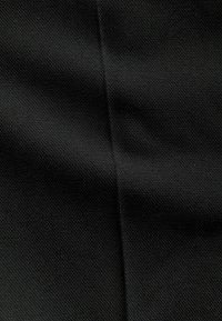 Tejido negro texturizado que presenta un sutil patrón de tejido diagonal, suave al tacto con un ligero brillo y costuras visibles.