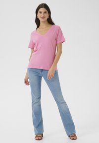 Rózsaszín pamut póló V nyakkal, rövid ujjú, laza szabású, világoskék trapéznadrággal és barna magassarkú szandálokkal párosítva.